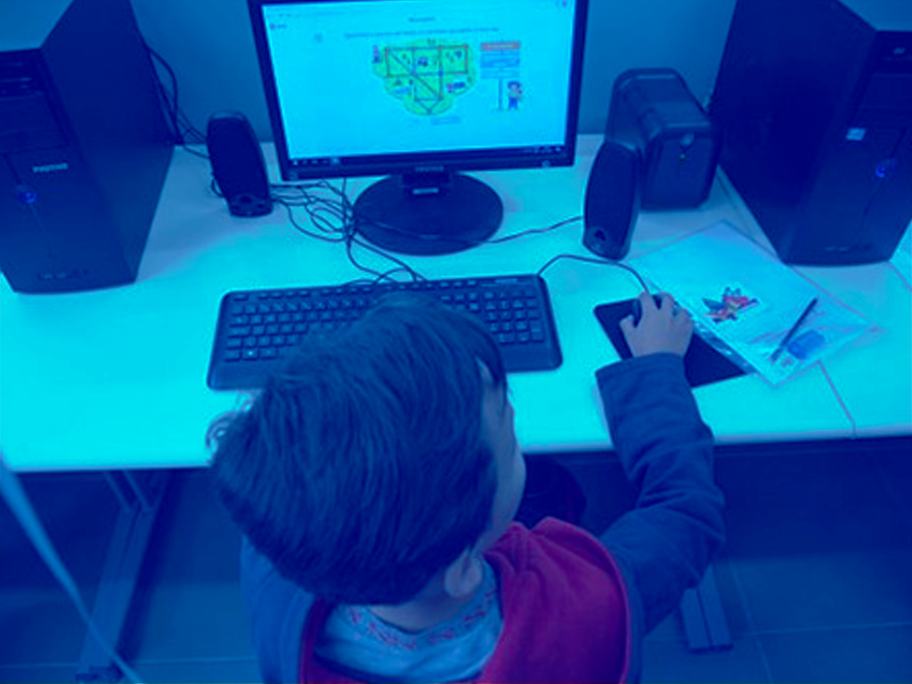 Criança mexendo em um computador visto de um ângulo a cima da criança em direção ao monitor