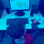 Criança mexendo em um computador visto de um ângulo a cima da criança em direção ao monitor